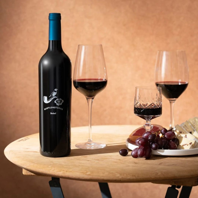 Bottle of Babylonstoren Shiraz red wine with two glasses on a wooden table against a warm background