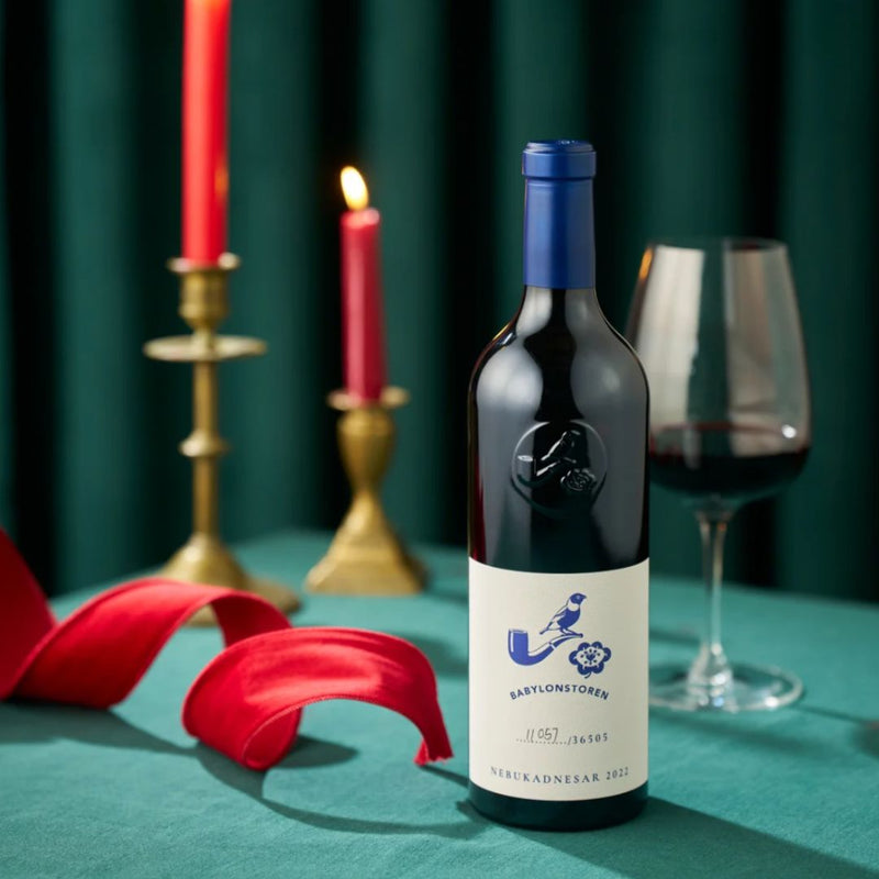 Bottle of Babylonstoren Nebukadnesar wine with a blue label on a green tablecloth with candles and a glass.