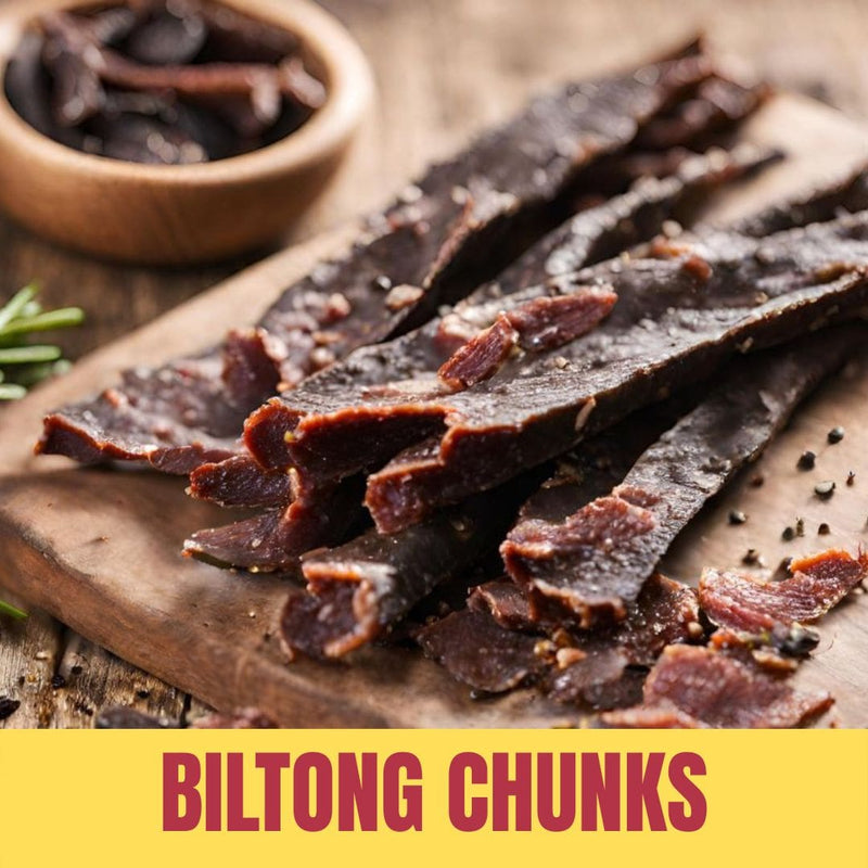 Biltong chunks on a wooden board with a bowl of additional biltong in the background.