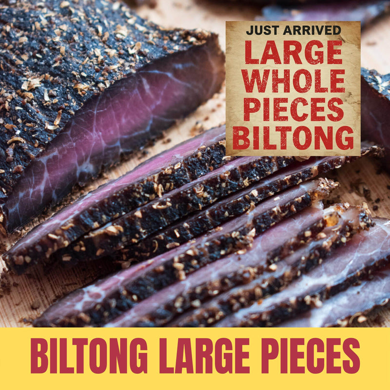 Large piece of biltong, sliced with a sign indicating 'Just Arrived Large Whole Pieces Biltong' on a wooden surface.