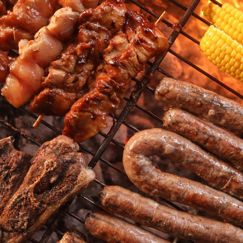 Grilled meats including sausages, chicken, and corn on the cob on a grill. Perfect Braai meats