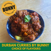 Blue bowl of Durban curry with Bunny Street Food branding on a wooden surface