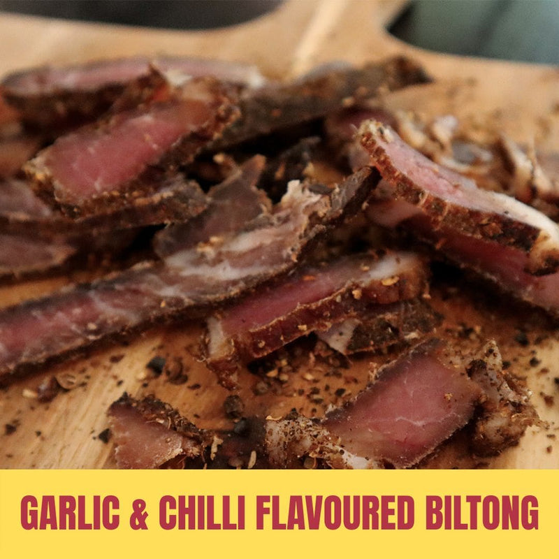 Sliced garlic & chilli flavoured biltong on a wooden board with text overlay.
