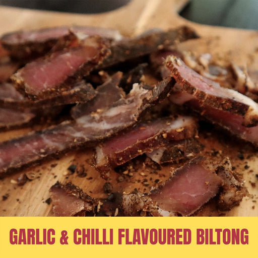 Sliced garlic & chilli flavoured biltong on a wooden board with text overlay.