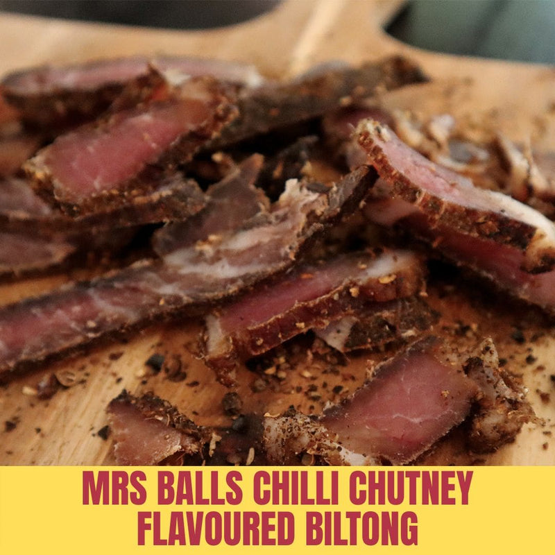 Sliced biltong with 'Mrs Balls Chilli Chutney Flavoured Biltong' text on a wooden board.